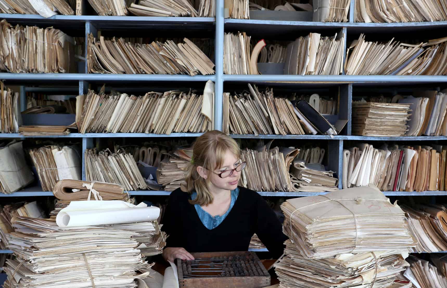 Frau sitzt zwischen Papierstapeln voller Finanzwissen